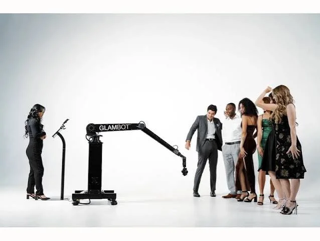 Group of dressed-up guests posing beside a Glambot arm and control stand in a white studio
