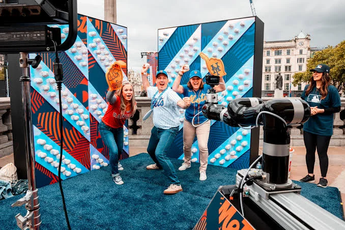 Cheering fans posing in front of a colourful backdrop with a robotic camera arm filming them