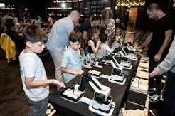 Children and adults gathered around robotic arms drawing portraits at an event